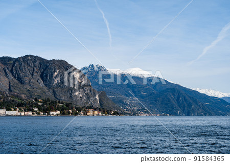 Town of Tremezzo against the backdrop of snow-capped mountain peaks. Italy, Lake Como  91584365
