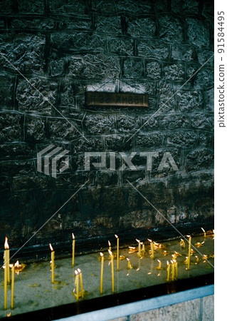 Wax candles burn on a pedestal near a stone wall in a temple Wax candles burn on a pedestal near a stone wall in a temple 91584495