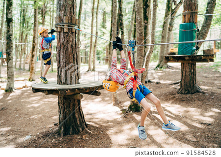 Boy climbs the zip line holding on to the safety ropes Boy climbs the zip line holding on to the safety ropes 91584528
