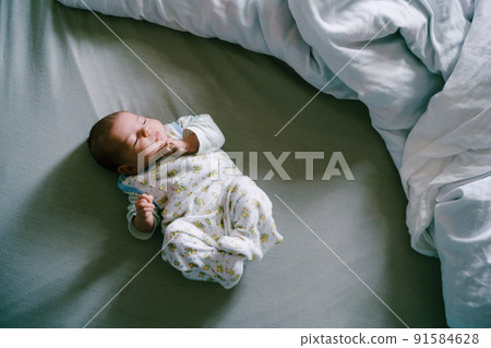 Infant in the crawlers sleeps on the bed, arms and legs bent. Top view Infant in the crawlers sleeps on the bed, arms and legs bent. Top view 91584628