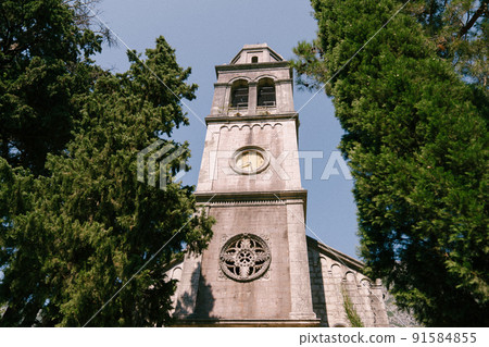 High stone bell tower with a clock among the trees 91584855