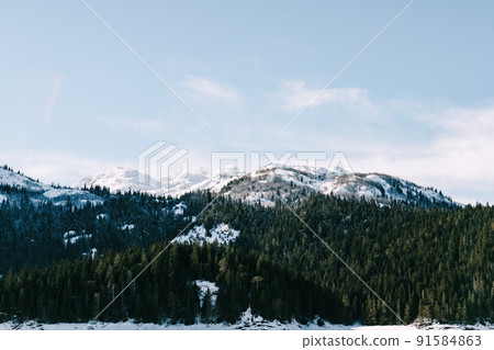 Black lake against the background of a green coniferous forest and snow-capped mountains. Montenegro 91584863