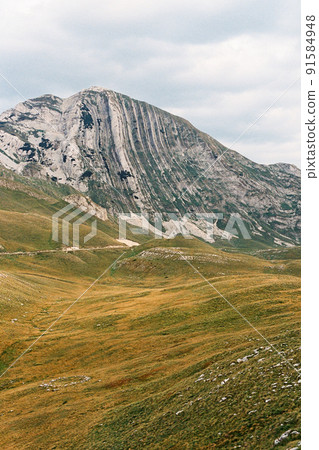 Rocky mountain looms over a green plain 91584948