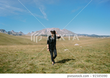 Young man walks through a valley holding his hat with his hand 91585090
