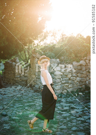 Woman in a straw hat stands by the ruins of a building holding the hem of her skirt 91585182