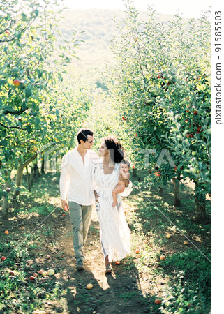 Man hugging a woman with a newborn in her arms walking in the garden 91585503