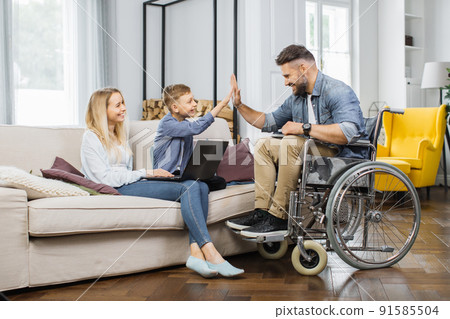 Child making high five gesture with disabled father at home 91585504