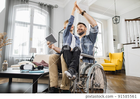 Boy giving high five to disabled dad with tablet at home Boy giving high five to disabled dad with tablet at home 91585561