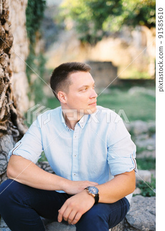 Young man sits on stone steps with his head turned to the side 91585610