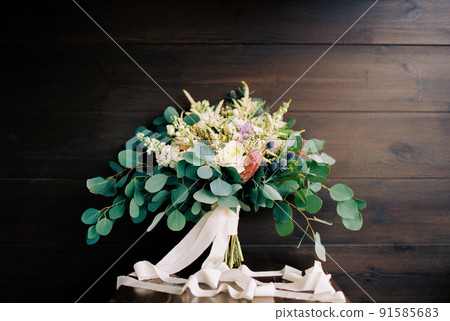 Wedding bouquet of flowers with green leaves and ribbons lies on a wooden table 91585683