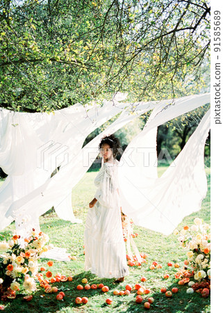Woman with bouquet near white curtains among trees Woman with bouquet near white curtains among trees 91585689