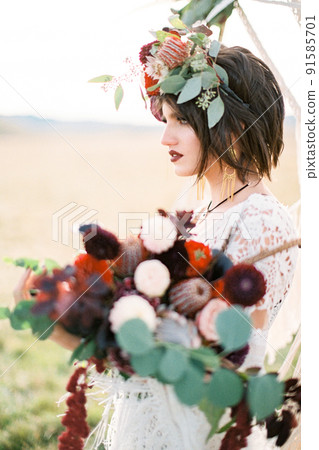 Bride in a wicker dress and a wreath with a bouquet of flowers in her hands 91585701