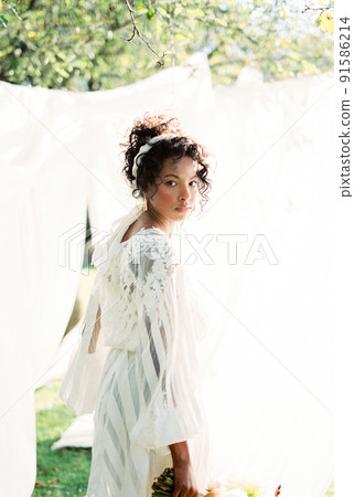 Woman in a dress stands near the white curtains in the garden 91586214