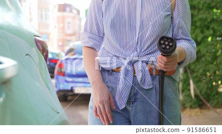 woman plugging in an electric car at outlet socket. 91586651