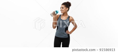 Healthy and Fitness concept - beautiful African American girl in sport clothes drinking water after workout. Isolated on white studio background Healthy and Fitness concept - beautiful African American girl in sport clothes drinking water after workout. Isolated on white studio background 91586913