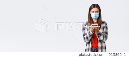 Coronavirus outbreak, lifestyle during social distancing and holidays celebration concept. Cute young woman in medical mask celebrating birthday alone during quarantine, hold b-day cake Coronavirus outbreak, lifestyle during social distancing and holidays celebration concept. Cute young woman in medical mask celebrating birthday alone during quarantine, hold b-day cake 91586941