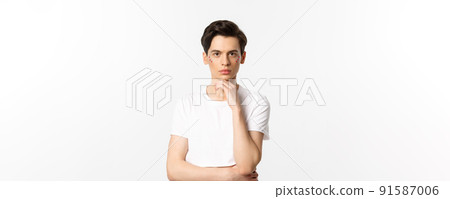 Image of attractive gay man in white t-shirt, having glitter on face and looking at camera serious, standing over white background 91587006