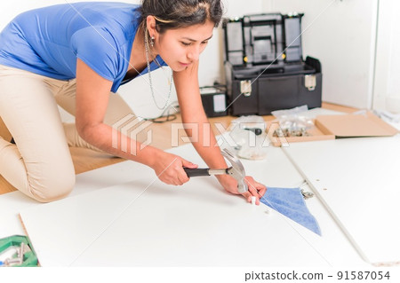 Latin Bolivian strong and independent success woman assembly and repair furniture with hammer. 91587054