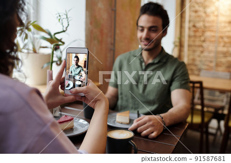 Hands of girl with mobile phone taking photo of her happy boyfriend 91587681