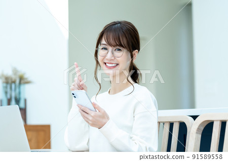 A woman with glasses who operates a smartphone while using a laptop computer 91589558