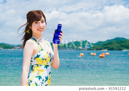Woman in a swimsuit drinking water at the beach Woman in a swimsuit drinking water at the beach 91591212