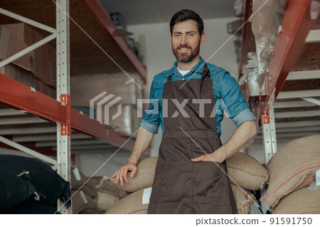 Warehouse worker standing near bags with coffee beans in the coffee small factory Warehouse worker standing near bags with coffee beans in the coffee small factory 91591750