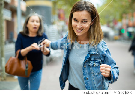 Woman thief trying to snatch smartphone from elderly woman outdoors 91592688
