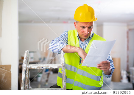 Man with documents in her hands stands in the middle of renovated room in cottage 91592995