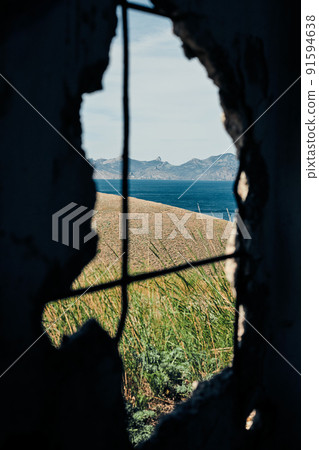The sea and the rocks on the south coast. Crimea, landscape on a sunny day. View through a hole in the wall. Vertical photo. The sea and the rocks on the south coast. Crimea, landscape on a sunny day. View through a hole in the wall. Vertical photo. 91594638