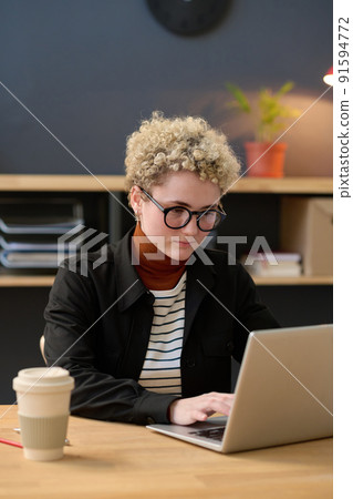 Young businesswoman in eyeglasses concentrating on her online work on laptop, she sitting at office desk with coffee cup Young businesswoman in eyeglasses concentrating on her online work on laptop, she sitting at office desk with coffee cup 91594772