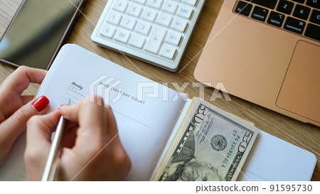 Woman counting money and making notes in notepad Woman counting money and making notes in notepad 91595730