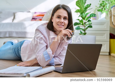 Attractive young woman looking at camera lying on floor at home with laptop Attractive young woman looking at camera lying on floor at home with laptop 91598069