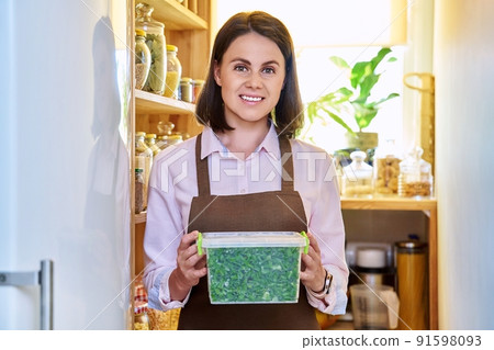 Woman with container of frozen green onions, in kitchen in pantry near freezer. Woman with container of frozen green onions, in kitchen in pantry near freezer. 91598093
