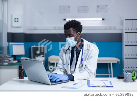 Healthcare facility expert using laptop to check patient record files. Clinic specialist prescribing medication while wearing virus protection facemask because of covid pandemic. Healthcare facility expert using laptop to check patient record files. Clinic specialist prescribing medication while wearing virus protection facemask because of covid pandemic. 91599082