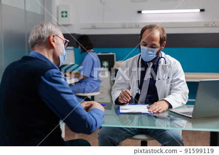 Practitioner putting medical seal on prescription paper to give health care medicine to senior man in office. Physician using stamp on checkup visit report during coronavirus pandemic. 91599119