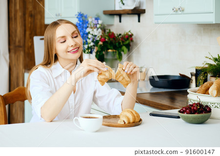 Smiling woman tears apart a fresh croissant 91600147