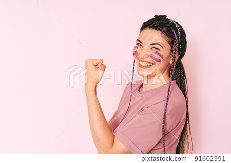 Girl with purple paint on her face clenching her fist against pink background Girl with purple paint on her face clenching her fist against pink background 91602991