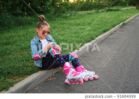 Pretty little girl learning to roller skate on beautiful summer day in a park. Pretty little girl learning to roller skate on beautiful summer day in a park. 91604099