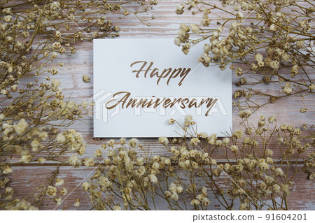 Happy Anniversary text on paper card with flower decoration on wooden background 91604201