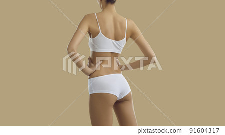 Backside of beautiful slim model posing in white underwear against beige background Backside of beautiful slim model posing in white underwear against beige background 91604317