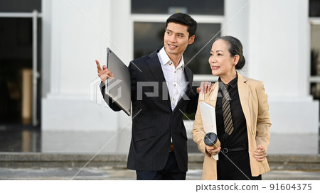 Two happy business people in formal suits walking in street with office building background 91604375