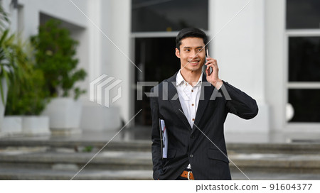 Handsome businessman in formal suits talking on mobile phone and standing outdoor with office building background Handsome businessman in formal suits talking on mobile phone and standing outdoor with office building background 91604377