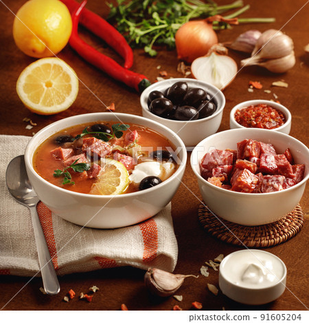 Meat Solyanka soup on with ingridients, sausage, olive,lemon, parsley, garlic, yogurt. Ukrainian food. Wooden background. Meat Solyanka soup on with ingridients, sausage, olive,lemon, parsley, garlic, yogurt. Ukrainian food. Wooden background. 91605204