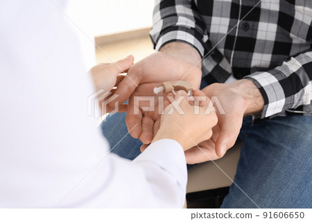 The doctor gives the hearing aid to the man, close up The doctor gives the hearing aid to the man, close up 91606650