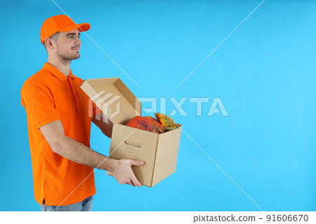 Delivery man holds box with pumpkins on blue background 91606670