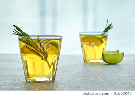 Two glass cups of kombucha are decorated with rosemary and lemon against the background of silhouettes of bamboo trees 91607045