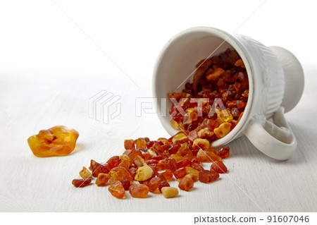 Raw amber spilled out on a wooden table from a white ceramic cup Raw amber spilled out on a wooden table from a white ceramic cup 91607046