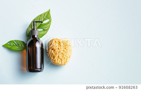 One cosmetic dark amber glass bottle with green plant and loofah on blue background 91608263
