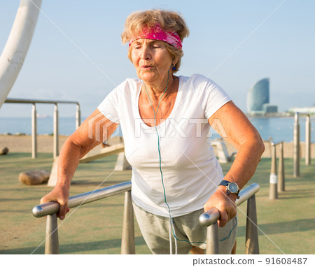 Mature lady exercising on dip station outdoors 91608487