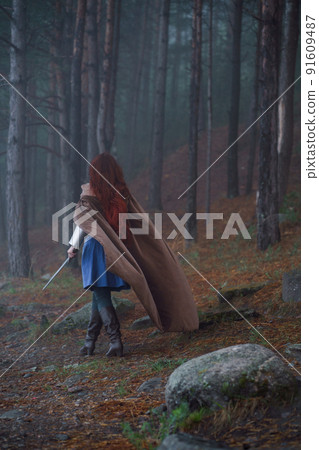 Young red-haired girl in medieval knight's armor in summer forest 91609487